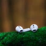 Close-up of wireless earbuds resting on vibrant green moss, showcasing portable audio technology.