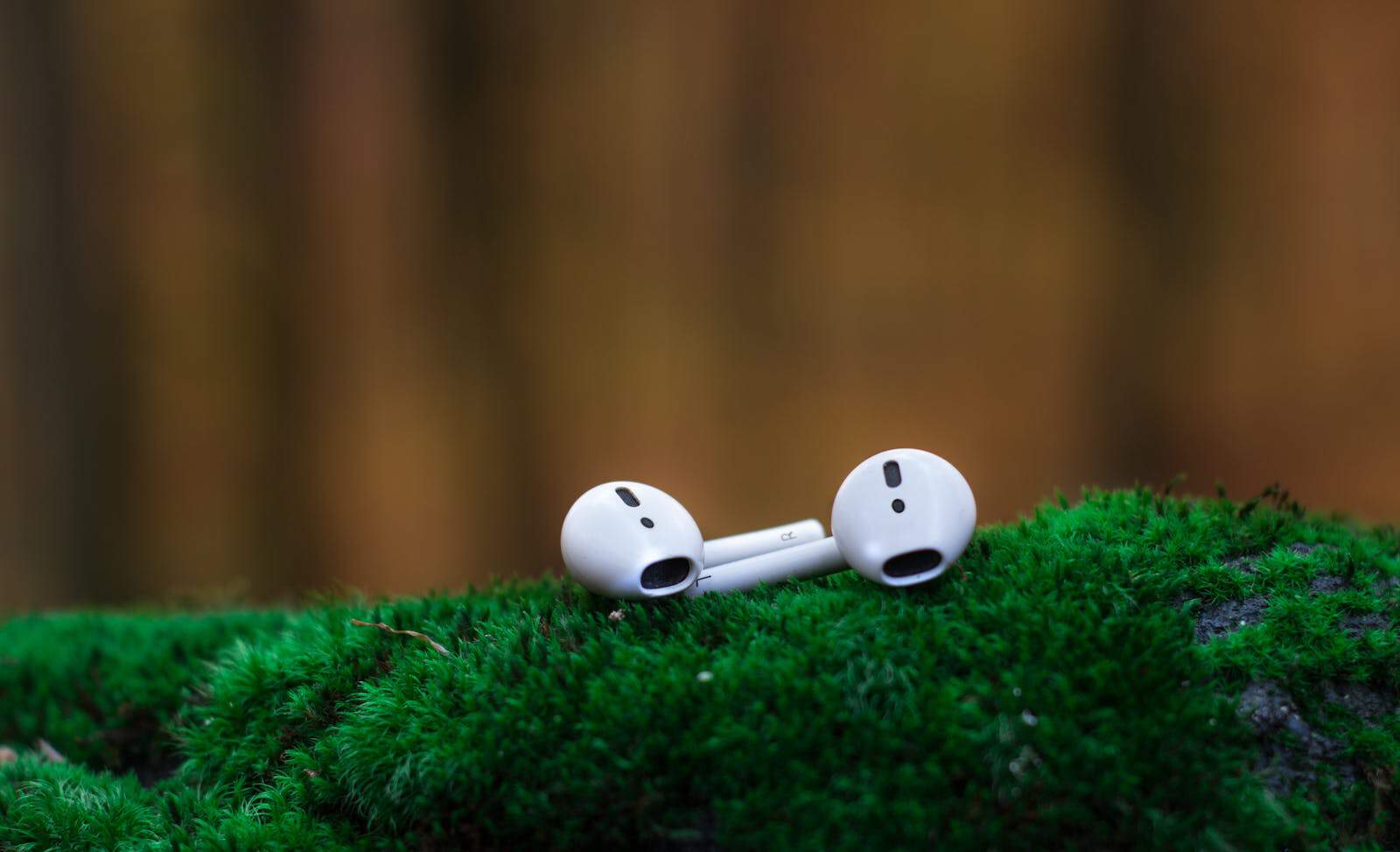 Close-up of wireless earbuds resting on vibrant green moss, showcasing portable audio technology.