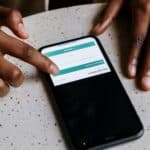 Close-up of hands interacting with a smartphone, displaying downloading interface.