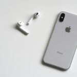 Close-up of a silver iPhone and wireless AirPods on a sleek white background.