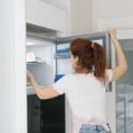 Woman with red hair opens a refrigerator in a modern kitchen, searching for food.