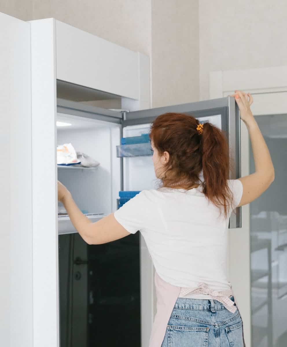 Woman with red hair opens a refrigerator in a modern kitchen, searching for food.