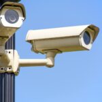 Outdoor security cameras mounted on a pole against a clear blue sky, ensuring vigilant surveillance.