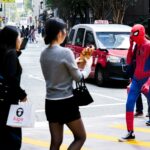 People taking pictures of spider-man crossing a street.