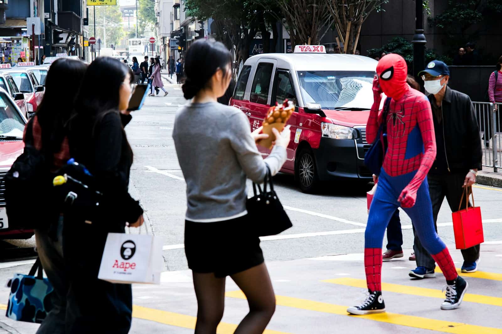 People taking pictures of spider-man crossing a street.